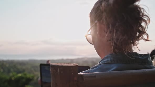 Freelancer woman sits with a laptop on a high bar chair. 