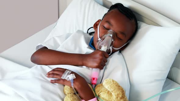 Sick girl in oxygen mask resting with teddy bear