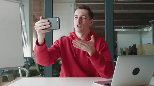 Portrait of Happy Man Making Facetime Video Calling with Smartphone at Modern Office Waving at