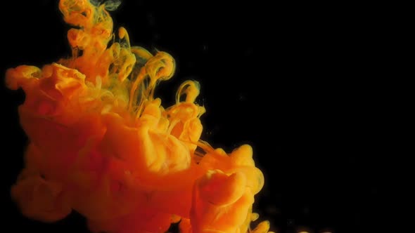 paint stream dissolves and spreads in water in water, orange colored ink cloud on black background