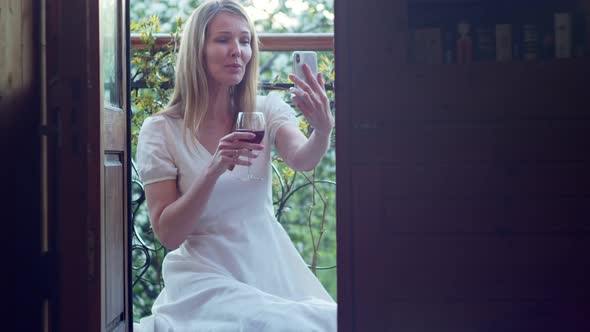 a Woman with a Glass of Wine on Her Balcony is Talking a Video Call in the Evening Twilight
