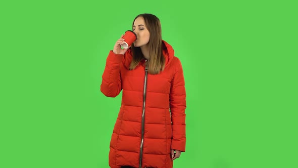 Lovely Girl in a Red Down Jacket Is Enjoying Coffee. Green Screen