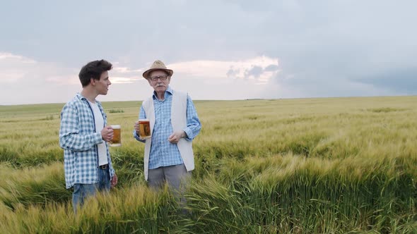 Two Men of Different Ages Hold Mugs with Beer and Talk When Admire the Nature