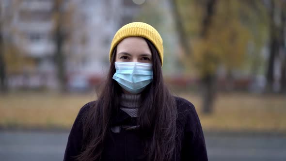 A Young Woman in a Protective Mask Walking in the Park Under Umbrella. Rainy Day, During Second Wave