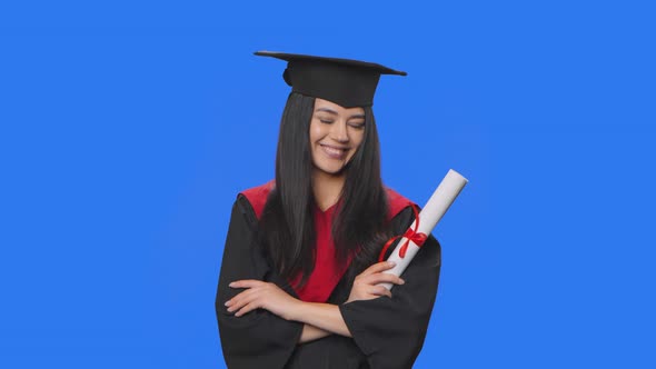 Portrait of Female Student in Cap and Gown Graduation Costume Smiling to Camera and Holding Her