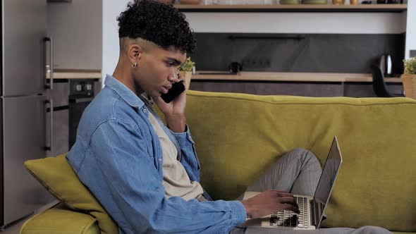 Young Afro Male Student Talking on Cell Phone While Working on Laptop at Modern Interior Background