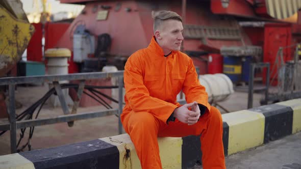 Young Man in Orange Uniform Sitting During His Break By the Sea in the Harbor