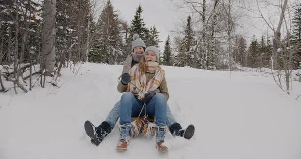 Dolly Shot of Happy Young Women Friends Sledding Down the Mountain in Winter Wood Laughing