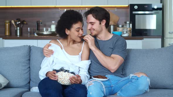 Beautiful Multiracial Couple in Love Sitting Next to Each Other on the Sofa with Bowl of Popcorn