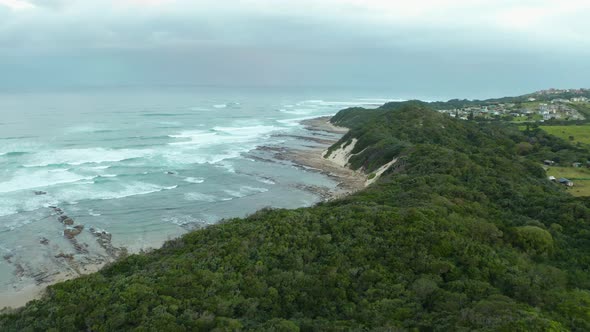 Aerial view, green sand dunes on a rocky beach & ocean waves crashing