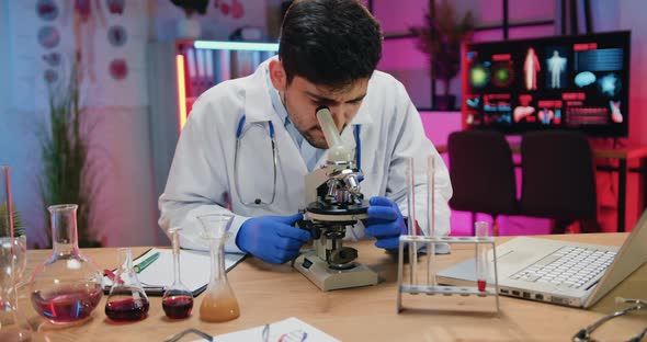 Chemist in white Coat Learning Samples Under Microscope in Evening Lab and Looking Into Camera