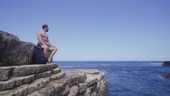 Man sitting on cliffs by the sea.