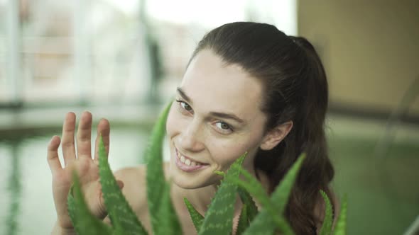 Young woman toucing aloe vera plant and laughing in health spa