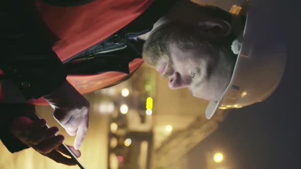 Vertical View of Engineer with Tablet Standing on Construction Site at Night.