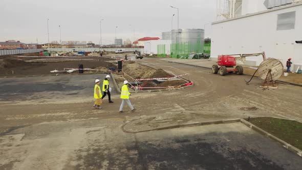 Employees in Vests Walk Along Construction Site Aerial View