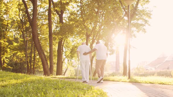 African-American caregiver is teaching disabled old man to walk with walker. Nurse and patient.