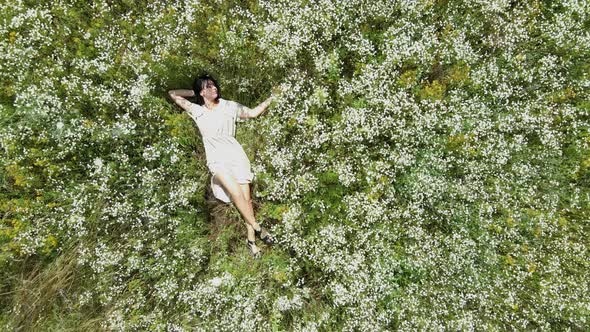 Drone aerial view of relax woman in dress lying on flower blooming meadow