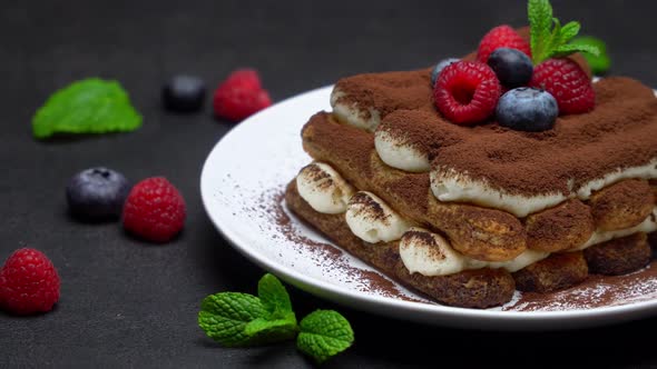 Portion of Classic Tiramisu Dessert with Raspberries and Blueberries on Dark Concrete Background