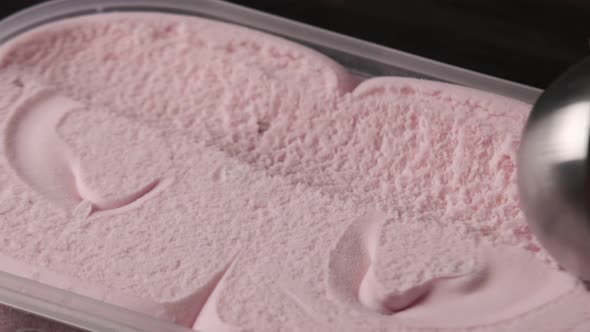 Close up view of a person scooping up fresh strawberry ice cream from tray.