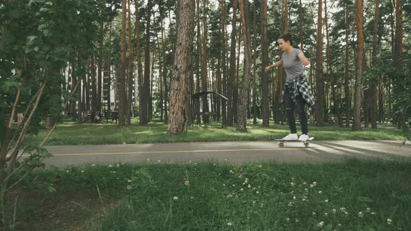 Young hipster woman trying to ride on skateboard in park, having fun, enjoying relaxed summer time.