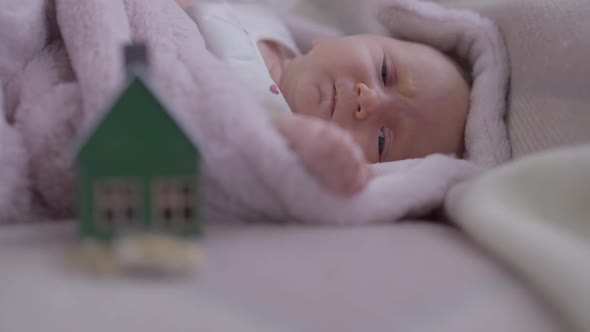 Portrait of Caucasian Infant Grimacing in Slow Motion with Blurred Toy House and Coins at Front on