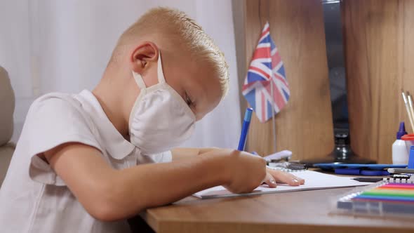 Boy Schoolboy in a Medical Mask Sits at Home in Quarantine and Does Homework