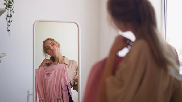 Woman Looks at Reflection in Mirror Choosing Dress for Party
