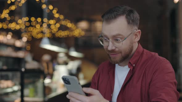 Businessman Sitting at the Cafe Looking at the Phone and Smiling While Rejoicing