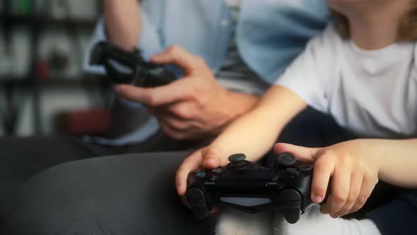 Hands of Unknown Father and Kid are Holding Wireless Controllers and Playing Video Game on Console