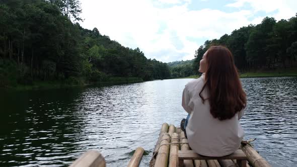 Rear view of a female traveler sitting and riding bamboo raft in the lake