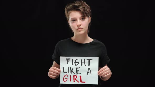 Released Serious Young Woman Posing with Fight Like a Girl Sign at Black Background