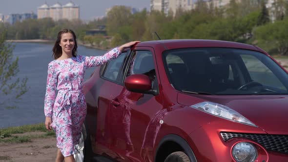 A Girl in a Flower Dress Walks Along the Car Looks Into the Frame Smiles and Spins