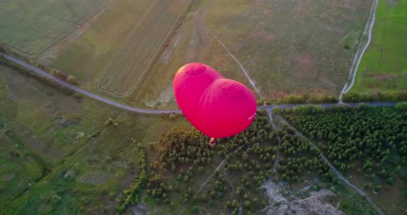 Red aerostat over fields. Romantic hot air balloon in a form of a heart travels in the sky on beauti