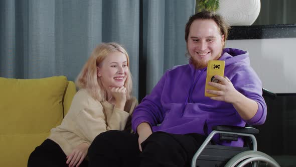 Young Couple of Blonde Woman and Man in a Wheelchair Talking with Somebody on Video Call