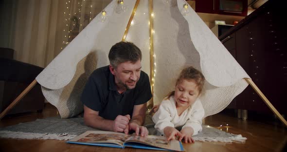 Dad and Daughter on Evening Play and Watch Cartoons on a Tablet in a Tent