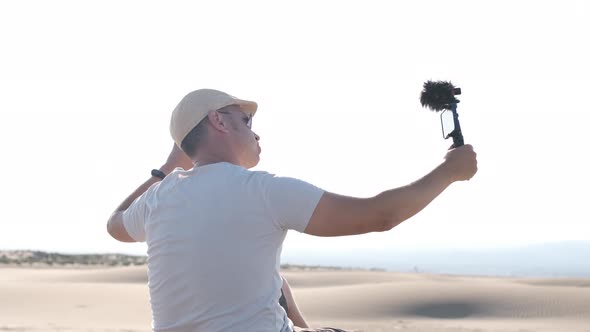 Man filming himself with his cell phone in the desert dunes, back side.