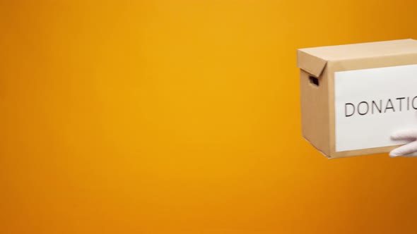 Human Hands Holding Cardboard Box with Coronavirus Donations Against Yellow Background