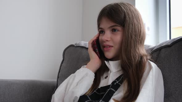 Little Young Girl Sitting on the Couch and Talking on the Phone