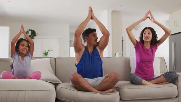 Hispanic parents and daughter sitting on the sofa meditating at home