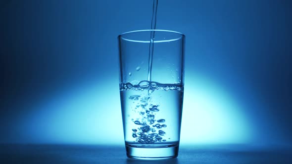 Pure Clear Water Is Poured Into a Glass on a Blue Background.