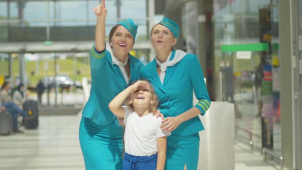 Charming Little Girl Standing with Stewardesses Next To Airport and Looking at Plane Takeoff