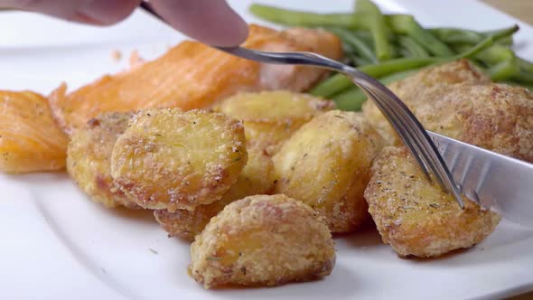 Slow Motion Slider Shot of Cutting into a Roast Potato on a White Plate With Green Beans and Salmon