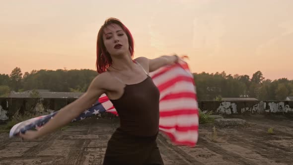 Young Woman with USA Flag Dancing on Roof at Sunset. US Independence Day.