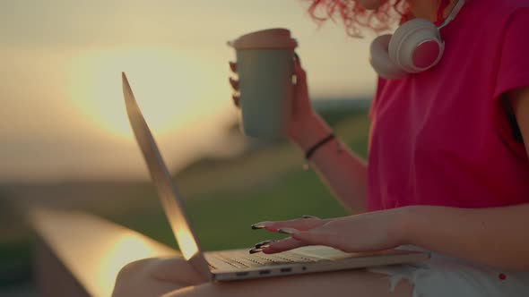 A Pink Curly Girl is Working or Studying on Laptop Outdoors alt