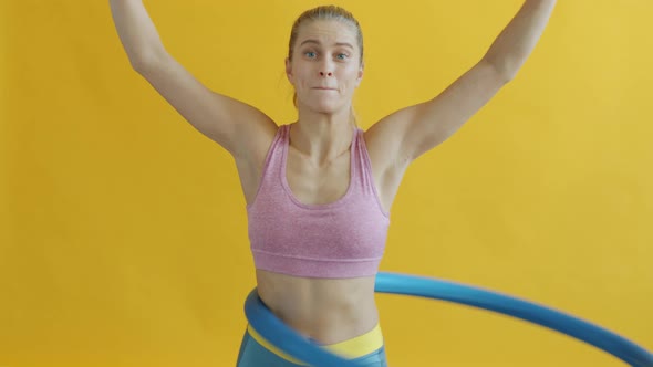 Slow Motion of Slender Woman Exercising with Hula Hoop Working Out Alone on Yellow Background