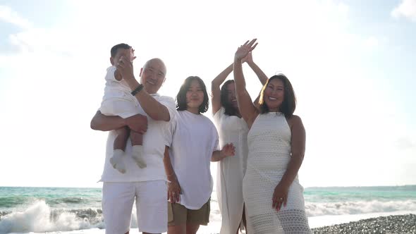 Joyful Asian Multigenerational Family Waving in Slow Motion Looking at Camera Standing in Sunlight