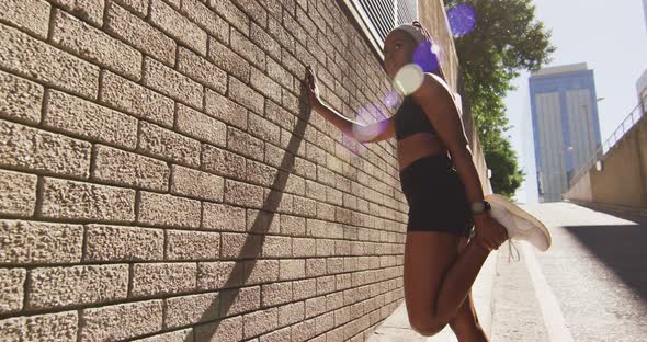 African american woman exercising outdoors leaning of wall and stretching in the city