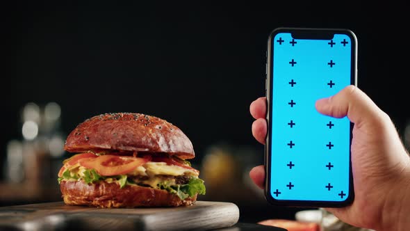 Tasty Burger and Smartphone with Blue Chroma Key Screen Closeup Cooked Juicy Sandwich Fast Food