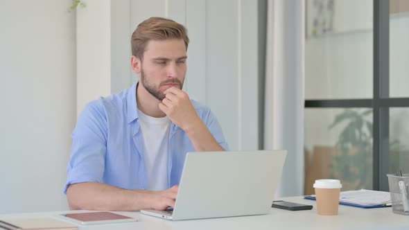 Thinking Young Creative Man Working on Laptop in Office