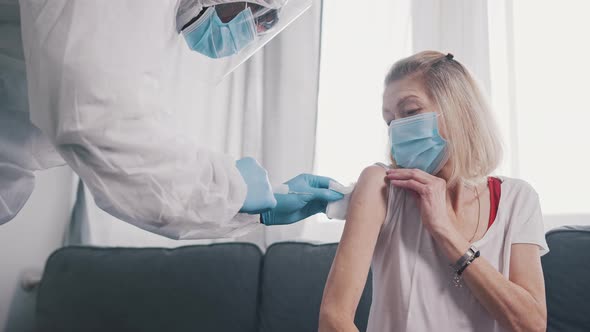 Nurse in Protective Suit Injecting Vaccine Against Covid Into the Arm of an Elderly Woman